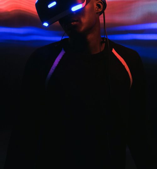 Portrait of an African American man wearing a VR headset, illuminated by neon lights.